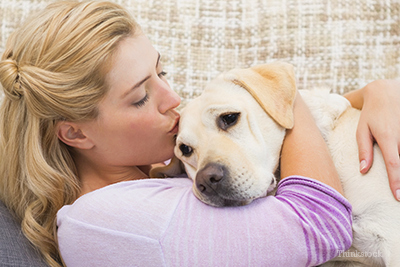 Woman on couch kissing dog